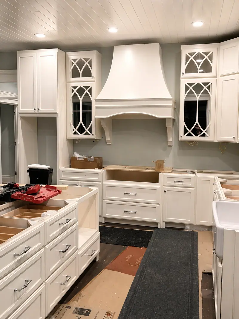 Kitchen mid-installation with custom cabinets, arched mullion glass, and a tall custom range hood