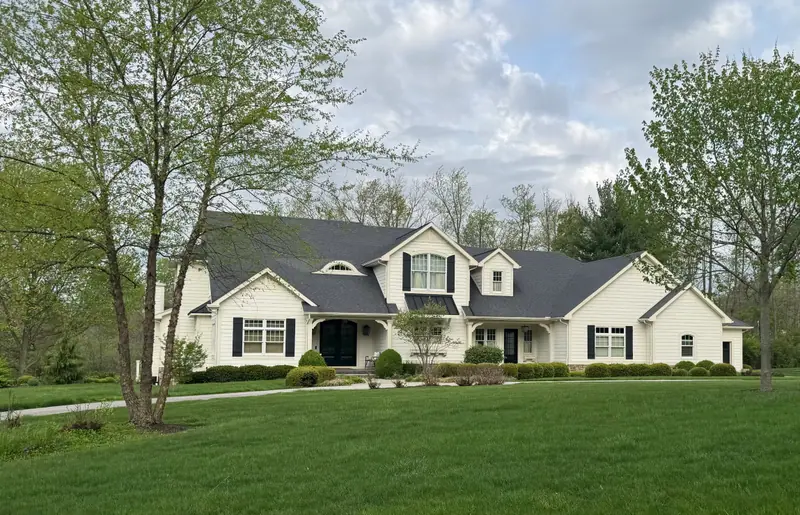 French Country custom home in Fort Wayne with cream siding, dark shutters, and arched entry