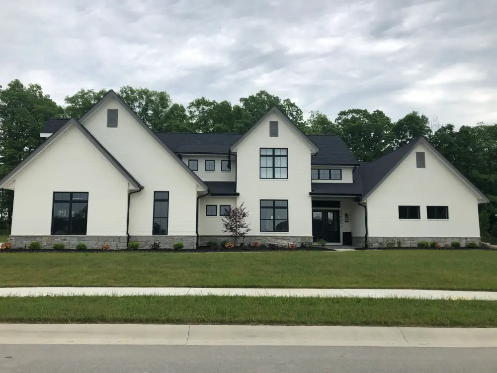 Modern farmhouse exterior with white siding, black windows, and stone base