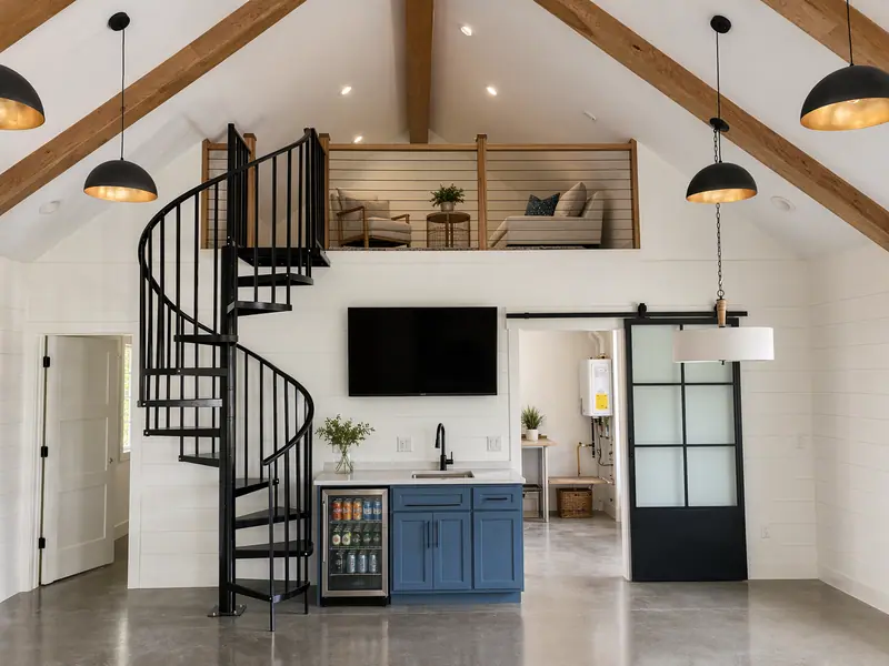 Open great room with vaulted white ceiling, black spiral staircase, and sleeping loft